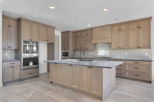 Kitchen featuring backsplash, appliances with stainless steel finishes, a kitchen island with sink, light stone countertops, and recessed lighting