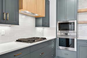 Kitchen featuring backsplash, stainless steel appliances, light stone counters, and gray cabinets