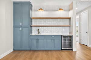 Indoor wet bar featuring blue cabinets, open shelves, backsplash, and recessed lighting