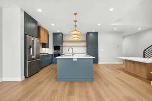 Kitchen with open shelves, a kitchen island with sink, appliances with stainless steel finishes, decorative light fixtures, and light wood-style flooring