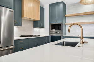 Kitchen with backsplash, stainless steel appliances, open shelves, ventilation hood, and light stone countertops