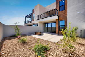 Back of property featuring a patio, stucco siding, a balcony, a fenced backyard, and an outdoor fire pit