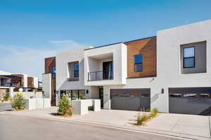 Contemporary house featuring a balcony, stucco siding, concrete driveway, and an attached garage