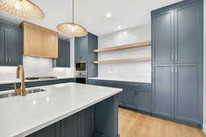Kitchen with decorative backsplash, open shelves, light wood-type flooring, hanging light fixtures, and recessed lighting