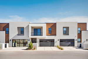 Contemporary house with a balcony, concrete driveway, stucco siding, and an attached garage