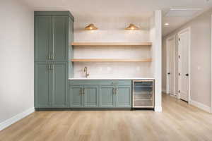 Indoor wet bar with green cabinets, beverage cooler, decorative backsplash, recessed lighting, and light wood-type flooring