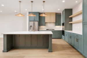 Kitchen with decorative backsplash, decorative light fixtures, green cabinets, a center island with sink, and recessed lighting