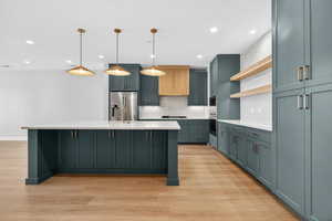 Kitchen with decorative backsplash, open shelves, pendant lighting, a kitchen island with sink, and appliances with stainless steel finishes