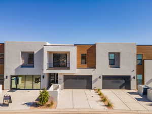 Contemporary house with a balcony, stucco siding, driveway, and a garage