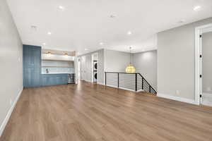 Unfurnished living room featuring beverage cooler, stacked washing machine and dryer, light wood-type flooring, and recessed lighting