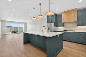 Kitchen featuring tasteful backsplash, light wood-style flooring, recessed lighting, a center island with sink, and pendant lighting