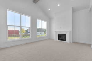Unfurnished living room with light colored carpet, high vaulted ceiling, a glass covered fireplace, beam ceiling, and recessed lighting