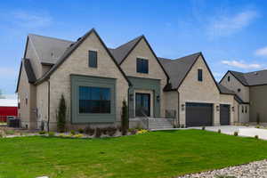 French provincial home with stone siding, a front yard, roof with shingles, and concrete driveway