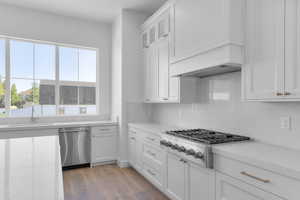 Kitchen featuring appliances with stainless steel finishes, white cabinets, decorative backsplash, light wood-style floors, and glass insert cabinets