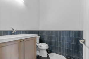 Bathroom featuring tile walls, vanity, a wainscoted wall, and dark tile patterned flooring