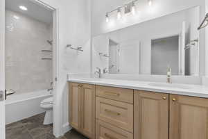 Bathroom featuring double vanity, washtub / shower combination, and dark marble finish flooring