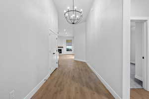 Hallway with recessed lighting, light wood-style flooring, a chandelier, and a towering ceiling
