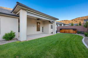Back of property with a hot tub, a ceiling fan, a patio area, stucco siding, and a mountain view