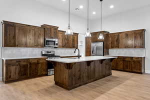 Kitchen featuring decorative backsplash, appliances with stainless steel finishes, hanging light fixtures, a breakfast bar, and light wood-style flooring
