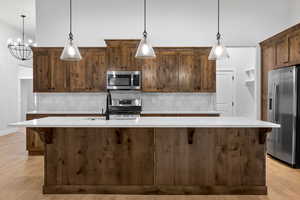 Kitchen with backsplash, light wood-style flooring, appliances with stainless steel finishes, and pendant lighting