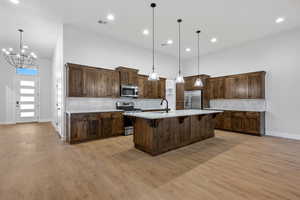 Kitchen featuring backsplash, appliances with stainless steel finishes, a kitchen bar, hanging light fixtures, and a center island with sink
