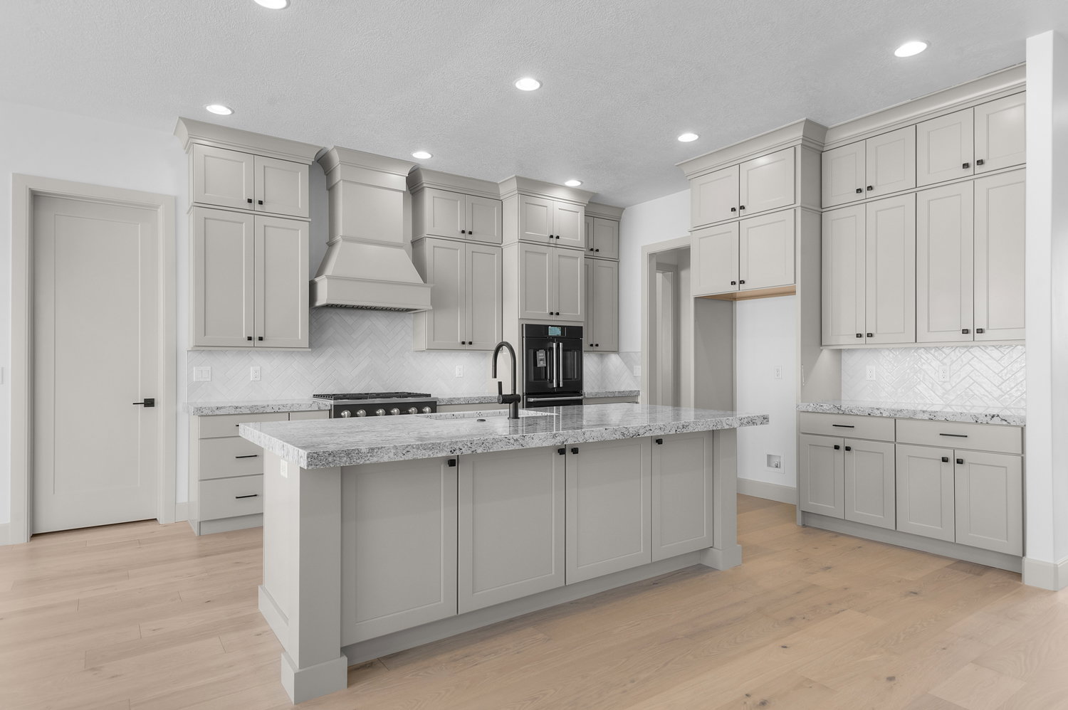 Kitchen with gray cabinetry, light stone counters, light wood-style flooring, a kitchen island with sink, and recessed lighting