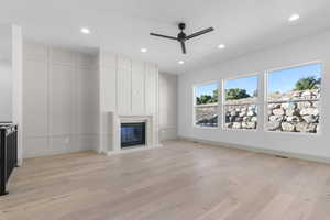 Unfurnished living room featuring light wood finished floors, a ceiling fan, a glass covered fireplace, recessed lighting, and a decorative wall