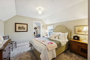 Carpeted bedroom featuring vaulted ceiling and a lit fireplace
