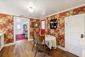 Dining room with wallpapered walls, wood-type flooring, and ornamental molding