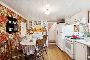 Kitchen with white appliances, glass insert cabinets, white cabinets, light countertops, and light wood-type flooring