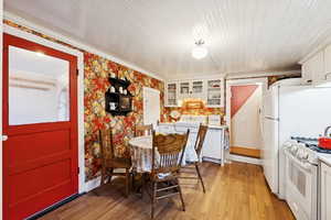 Dining space with light wood finished floors, crown molding, and wallpapered walls