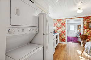 Laundry room with wallpapered walls, light wood finished floors, and stacked washing machine and dryer