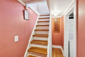 Stairway featuring wood finished floors, crown molding, and estacked washer and dryer