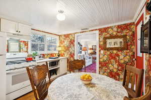 Dining room featuring light wood-type flooring, wallpapered walls, ornamental molding, and wood ceiling