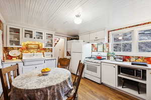 Kitchen with white cabinets, white appliances, light countertops, glass insert cabinets, and light wood-style floors