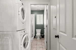 Laundry room featuring light tile patterned flooring, stacked washer and clothes dryer, and electric panel