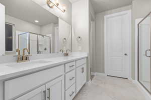 Full bathroom featuring double vanity, a stall shower, and light marble finish floors