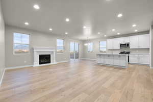 Kitchen featuring white cabinets, recessed lighting, open floor plan, an island with sink, and a glass covered fireplace