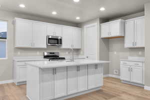 Kitchen with white cabinetry, recessed lighting, light wood-style flooring, stainless steel appliances, and light stone counters