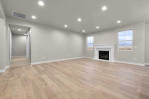 Unfurnished living room with recessed lighting, light wood-style floors, and a glass covered fireplace