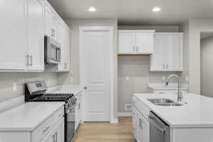 Kitchen featuring appliances with stainless steel finishes, white cabinetry, light wood-style flooring, recessed lighting, and light stone counters