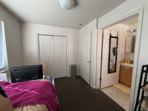 Bedroom featuring a textured ceiling, a closet, light carpet, and ensuite bath