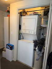 Laundry room featuring stacked washing machine and dryer and carpet flooring