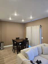 Living room with light wood colored flooring and recessed lighting looking into dining area