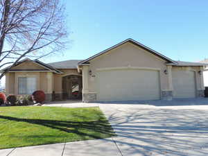 Single story home featuring stone siding, stucco siding, driveway, a front lawn, and an attached garage