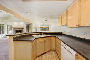 Kitchen with a textured ceiling, light brown cabinetry, open floor plan, dark countertops, and a tile fireplace