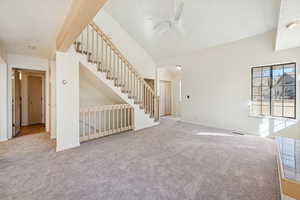 Unfurnished living room featuring light colored carpet, a ceiling fan, and stairway