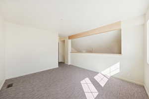 Spare room featuring carpet flooring and vaulted ceiling