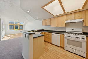 Kitchen featuring a textured ceiling, white appliances, light brown cabinets, dark countertops, and lofted ceiling