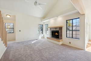 Unfurnished living room with high vaulted ceiling, light carpet, a ceiling fan, and a tiled fireplace